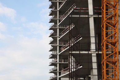 Photo of Construction site with tower crane near unfinished building under cloudy sky. Space for text