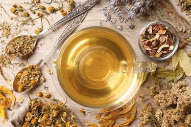Glass cup of aromatic freshly brewed tea near different dry herbs on wooden table, flat lay