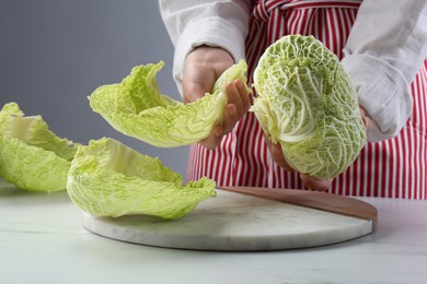 Woman separating leaf from fresh savoy cabbage at white marble table, closeup