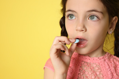 Little girl taking vitamin pill on yellow background, closeup. Space for text