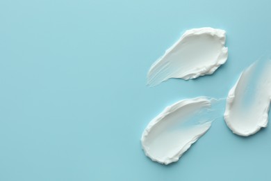 Samples of face cream on light blue background, top view. Space for text