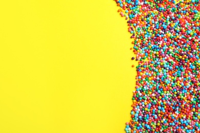 Bright colorful sprinkles on yellow background, flat lay with space for text. Confectionery decor
