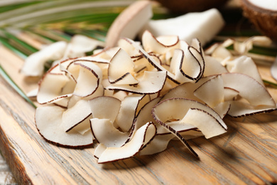 Pile of tasty coconut chips on wooden board, closeup