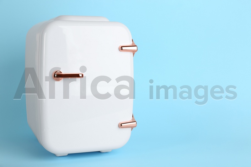 White cosmetics refrigerator on light blue background, space for text