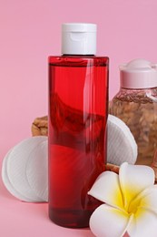 Bottles of micellar water, plumeria flower and cotton pads on pink background
