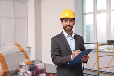 Professional engineer in hard hat with clipboard indoors