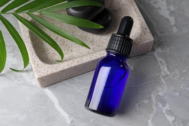 Bottle of face serum, soap dish, leaf and spa stones on grey marble table
