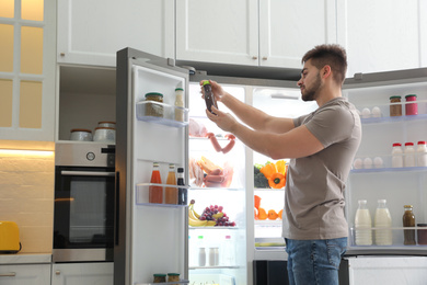 Young man with bottle of sauce near open refrigerator in kitchen