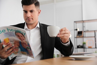 Man with cup reading magazine at table in office