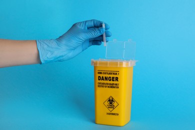 Doctor throwing used syringe needle into sharps container on light blue background, closeup