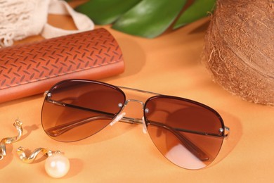 Photo of Stylish sunglasses and brown leather case on pale orange background