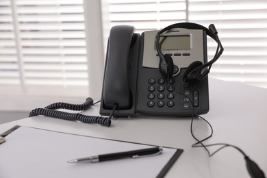 Desktop telephone with headset on white table in office. Hotline service