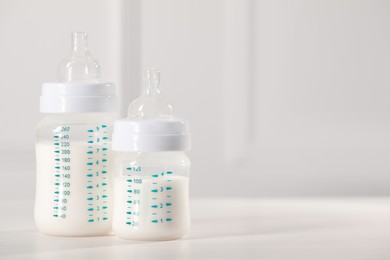 Photo of Feeding bottles with milk on white wooden table. Space for text
