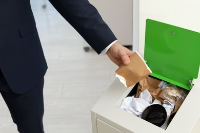 Man putting used paper cup into trash bin in office, closeup. Waste recycling