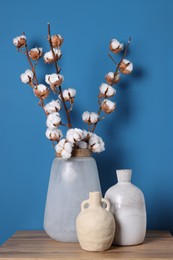 Vases and cotton branches on wooden table against light blue background