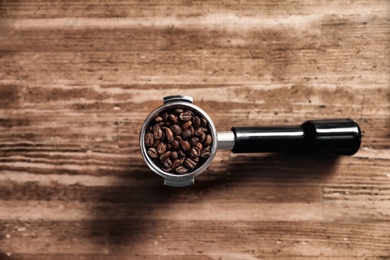 Portafilter with roasted coffee beans on wooden table, top view
