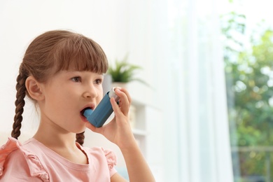 Little girl using asthma inhaler on blurred background
