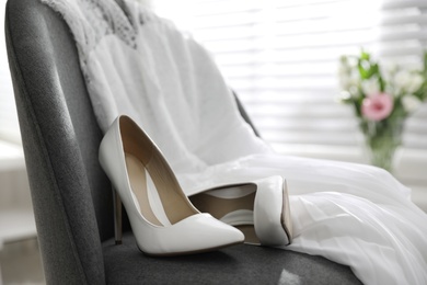 Pair of white high heel shoes and wedding dress on chair indoors