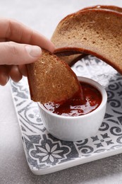 Woman dipping crispy rusk in sauce at light table, closeup