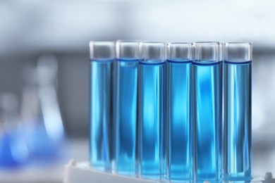 Test tubes with light blue liquid on blurred background, closeup