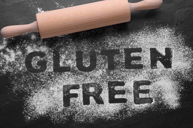 Rolling pin and phrase Gluten free written with flour on black table, flat lay