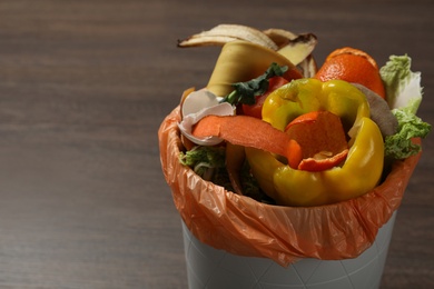 Trash bin with organic waste for composting on wooden background, closeup