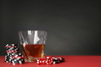 Casino chips, dice and whiskey on red table, space for text