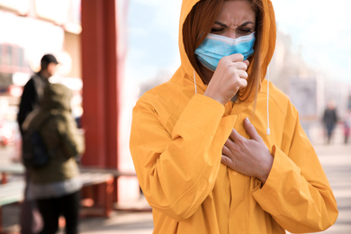 Woman with medical mask coughing on city street. Virus protection