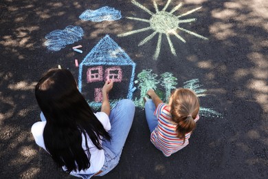 Little child and her mother drawing with colorful chalks on asphalt, above view