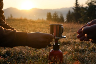 People making hot drink with portable gas burner in mountain camping, closeup