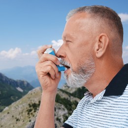 Image of Mature man using asthma inhaler in mountains. Emergency first aid during outdoor recreation