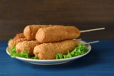 Delicious deep fried corn dogs with lettuce leaves on blue wooden table