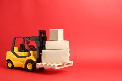 Toy forklift with wooden pallet and boxes on red background, space for text