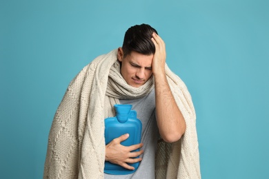 Ill man with hot water bottle suffering from cold on light blue background