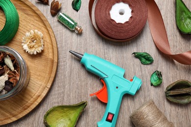 Photo of Hot glue gun and handicraft materials on wooden table, flat lay