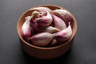 Unpeeled garlic cloves in wooden bowl on grey background