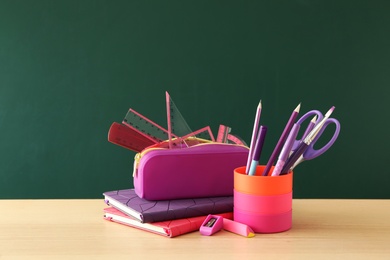 Different school stationery on wooden table near green chalkboard. Back to school