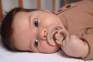 Cute little baby with pacifier lying in comfortable crib at home, closeup. Bedtime