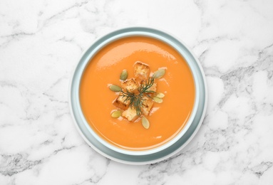 Tasty creamy pumpkin soup with croutons, seeds and dill in bowl on white marble table, top view