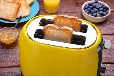 Yellow toaster with roasted bread, blueberries and jam on wooden table, closeup