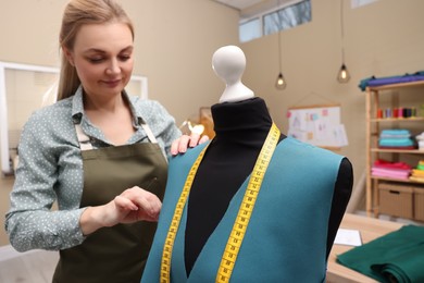 Dressmaker working with fabric in atelier, focus on mannequin