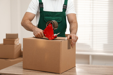 Man packing box with adhesive tape indoors, closeup. Moving service