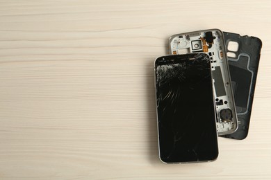 Parts of broken smartphone on white wooden table, flat lay with space for text. Device repair