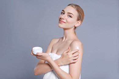 Young woman with jar of body cream on color background