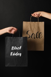 People holding paper bags with phrases Black Friday and Sale against dark background, closeup