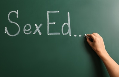Woman writing text "SEX ED..." on green chalkboard