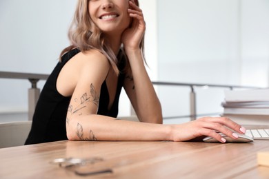 Photo of Beautiful woman with tattoos on arms using computer at table indoors, closeup