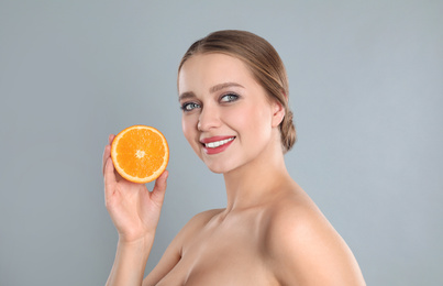 Young woman with cut orange on grey background. Vitamin rich food