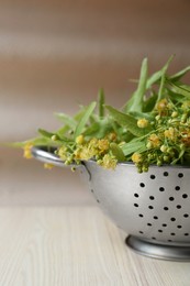 Photo of Beautiful linden blossoms and green leaves in metal colander on white wooden table, closeup
