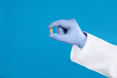 Doctor holding suppository for hemorrhoid treatment on blue background, closeup
